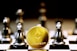 A gold Ethereum token is prominently placed on a black and white chessboard surrounded by several metallic chess pieces. The focus is on the Ethereum symbol on the coin, while the chess pieces appear slightly out of focus in the background. The lighting emphasizes the reflective surfaces of both the coin and the chess pieces.