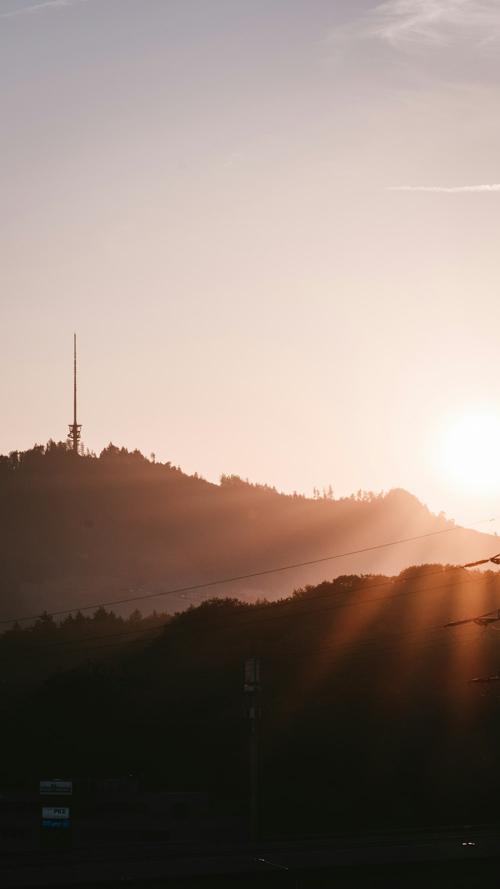 the sun is setting over a hill with a radio tower in the distance