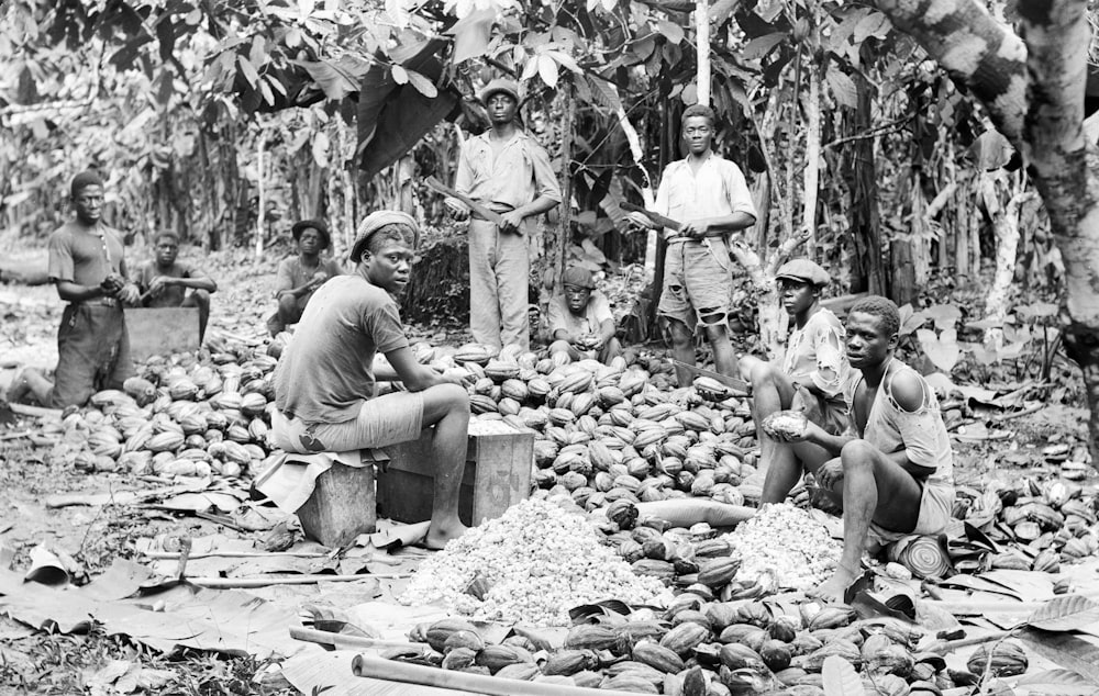 a group of men standing around a pile of fruit