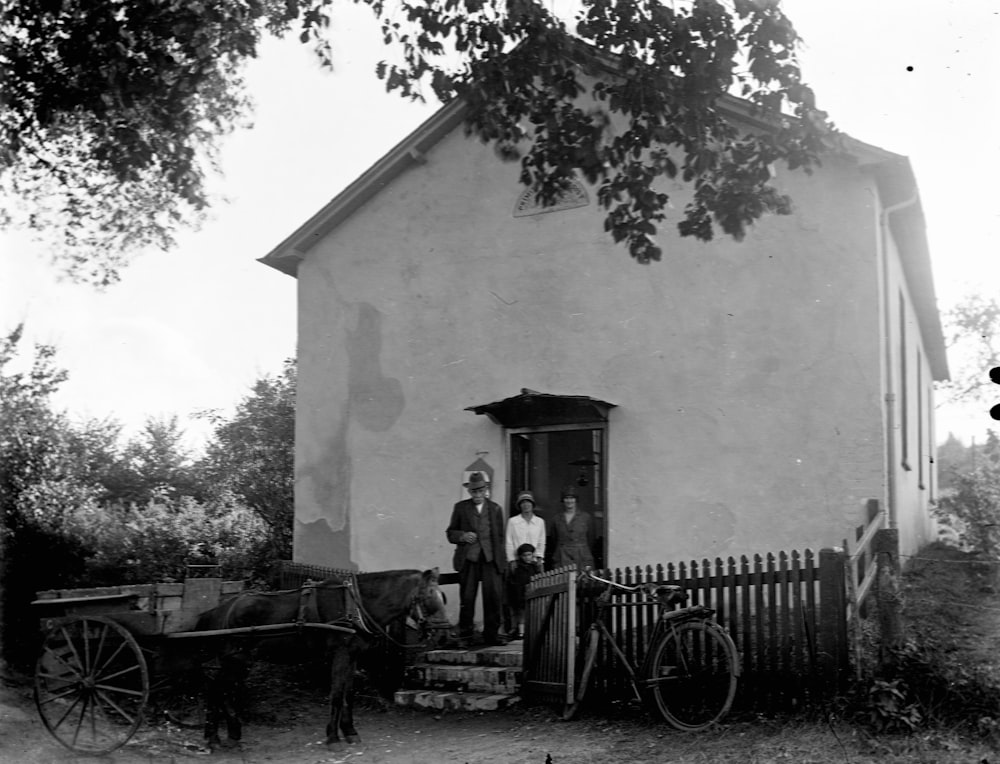 a black and white photo of people standing outside of a house