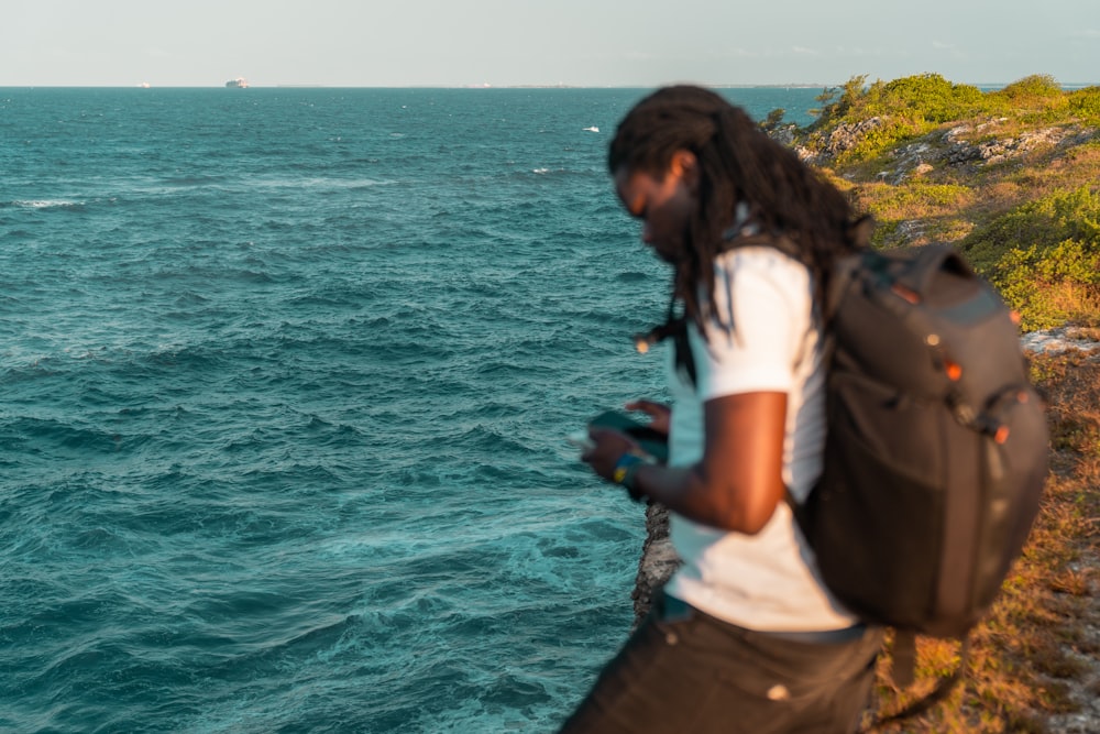 a man with dreadlocks standing on a cliff overlooking the ocean