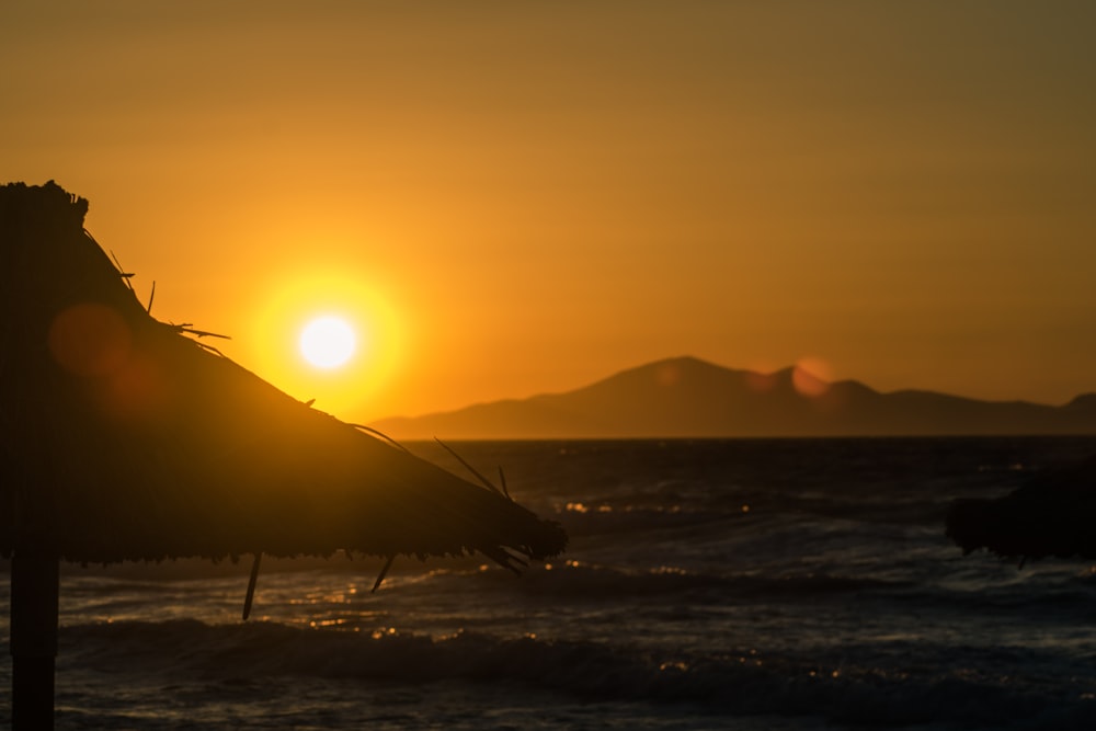 the sun is setting over the ocean with a beach umbrella