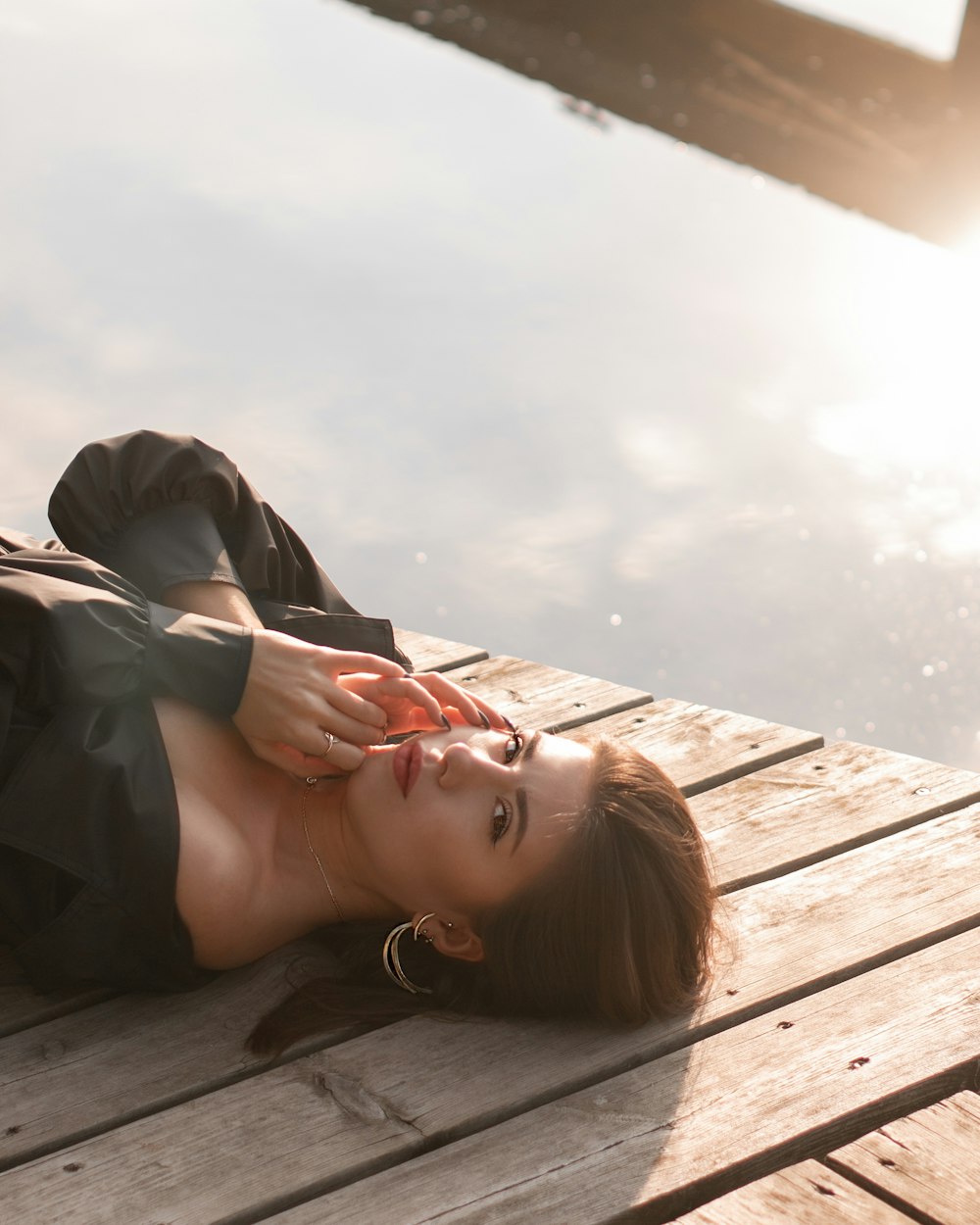 uma mulher deitada em uma doca de madeira ao lado de um corpo de água