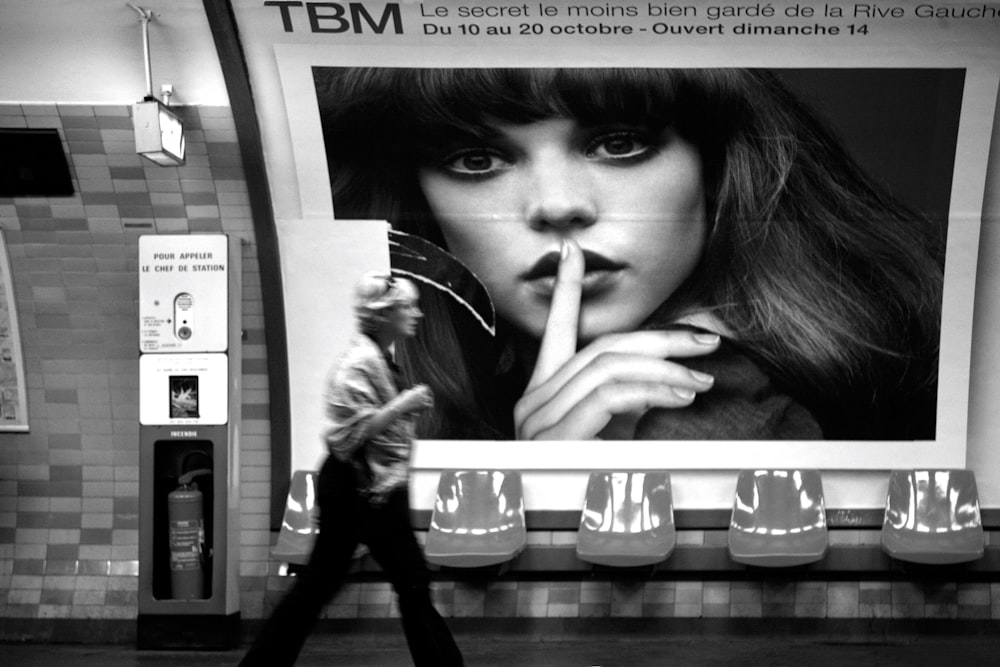 a woman walks past a billboard with a picture of a woman smoking a cigarette