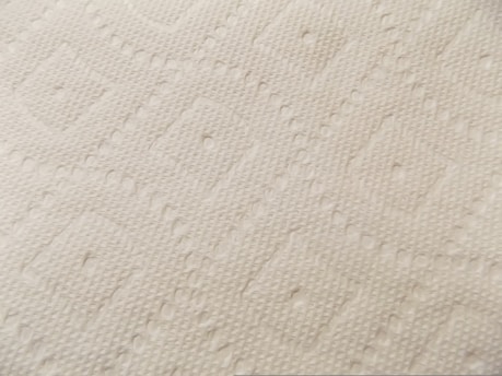 A close-up view of a textured surface, possibly a fabric or paper material, with an embossed diamond pattern. The surface appears soft with small raised dots and linear designs throughout, giving it a tactile appearance.