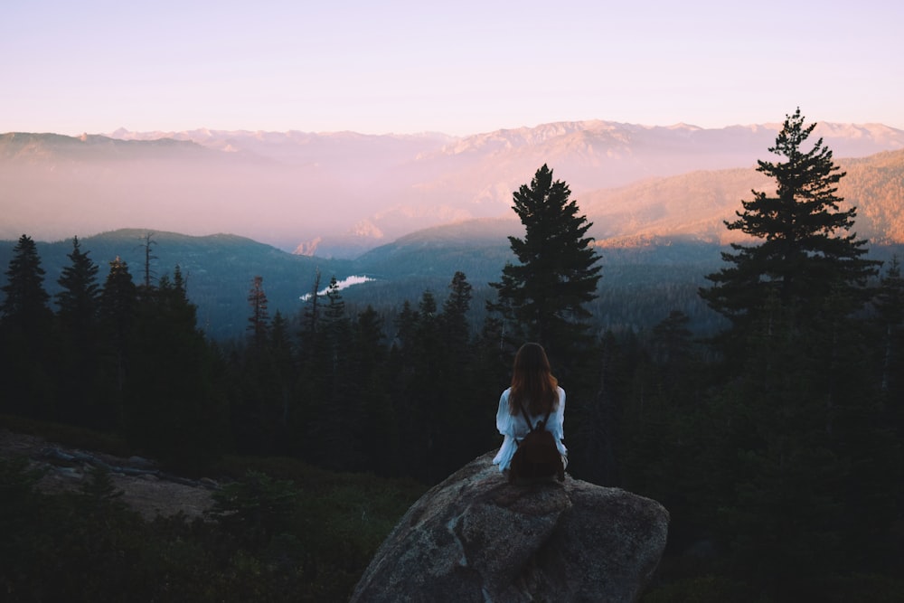 a woman sitting on top of a large rock