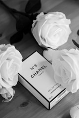 A timeless black and white portrait of a classic Chanel quilted purse resting on a white marble slab with soft gold accents around.