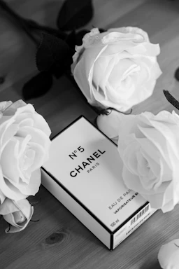 A minimalist black and white photo of a vintage perfume bottle surrounded by delicate dried flowers on a clean white surface.