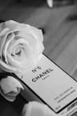 A black and white image features a perfume box labeled No. 5 Chanel Paris surrounded by elegant roses. The luxurious aesthetic is highlighted by the classic and timeless brand presentation.