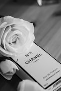 A black and white image features a perfume box labeled No. 5 Chanel Paris surrounded by elegant roses. The luxurious aesthetic is highlighted by the classic and timeless brand presentation.