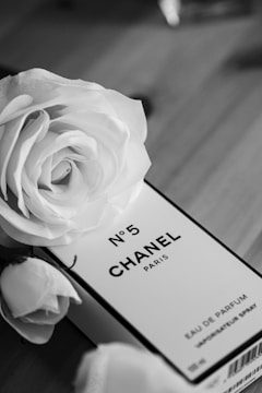 A black and white image features a perfume box labeled No. 5 Chanel Paris surrounded by elegant roses. The luxurious aesthetic is highlighted by the classic and timeless brand presentation.