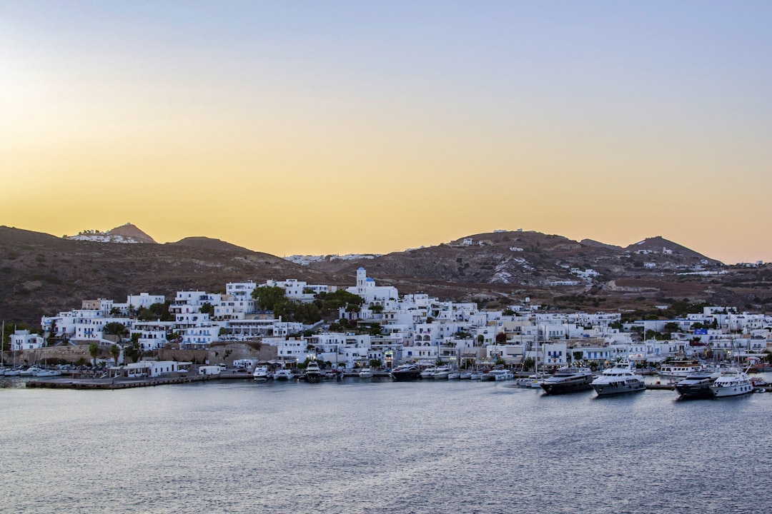 a group of boats floating on top of a body of water, The hills of Milos Island and the sky