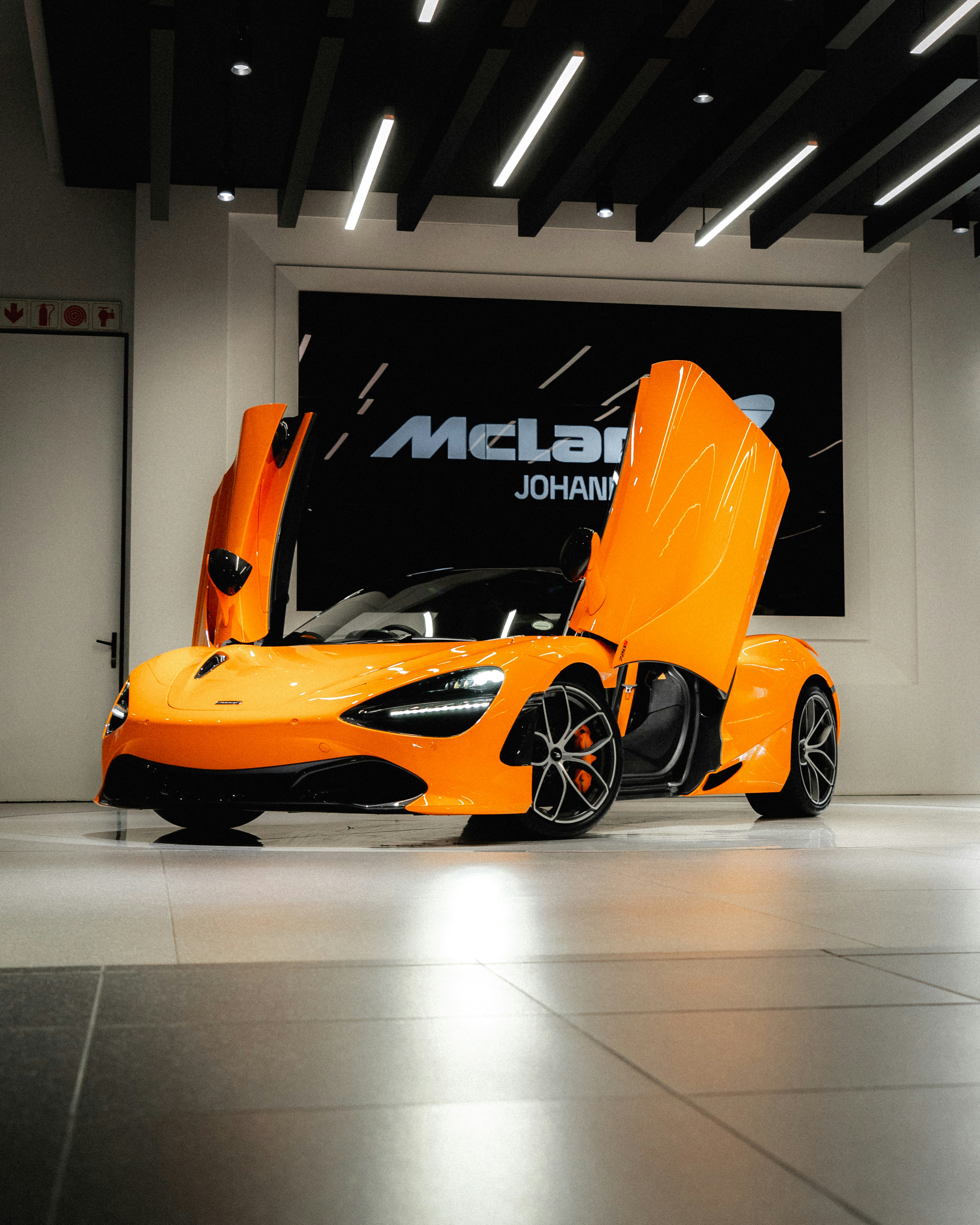 McLaren Artura hybrid supercar in deep orange, sleek aerodynamic body, dark moody showroom environment
