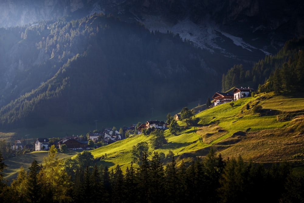 a small village on a green hillside surrounded by mountains