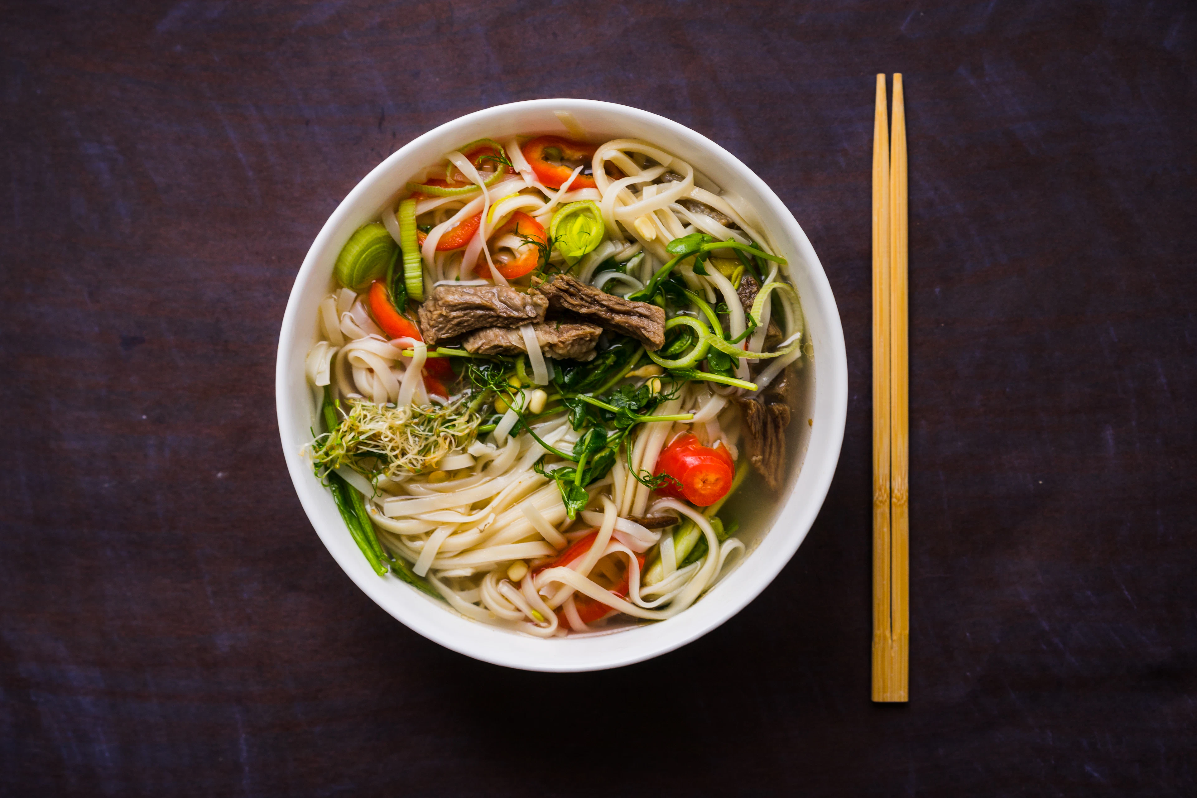 A rich Vietnamese noodle soup lifted with chopsticks under warm light