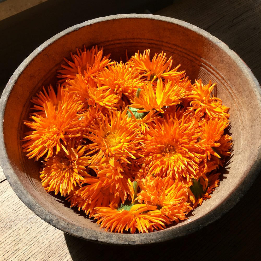 Un cuenco lleno de flores naranjas encima de una mesa de madera