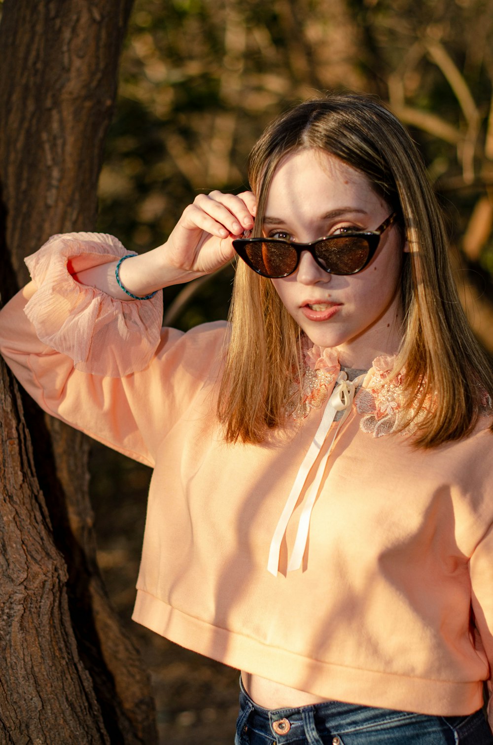 a woman wearing sunglasses standing next to a tree