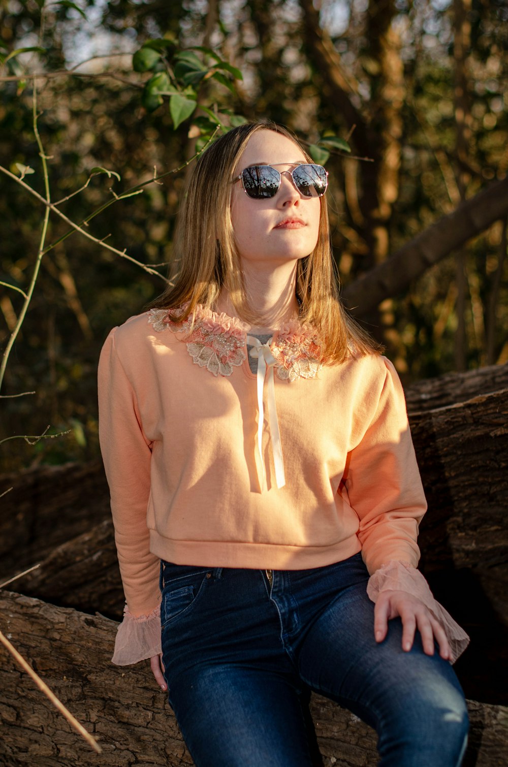 a woman sitting on a tree branch wearing sunglasses