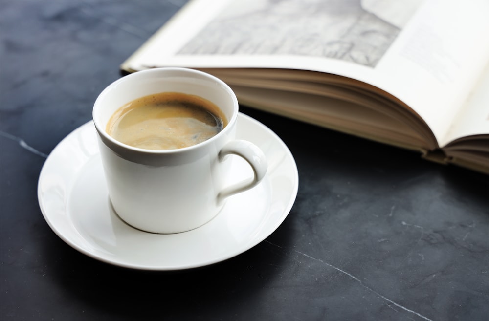 a cup of coffee on a saucer next to an open book