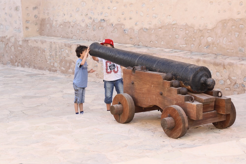a young boy standing next to a wooden cannon