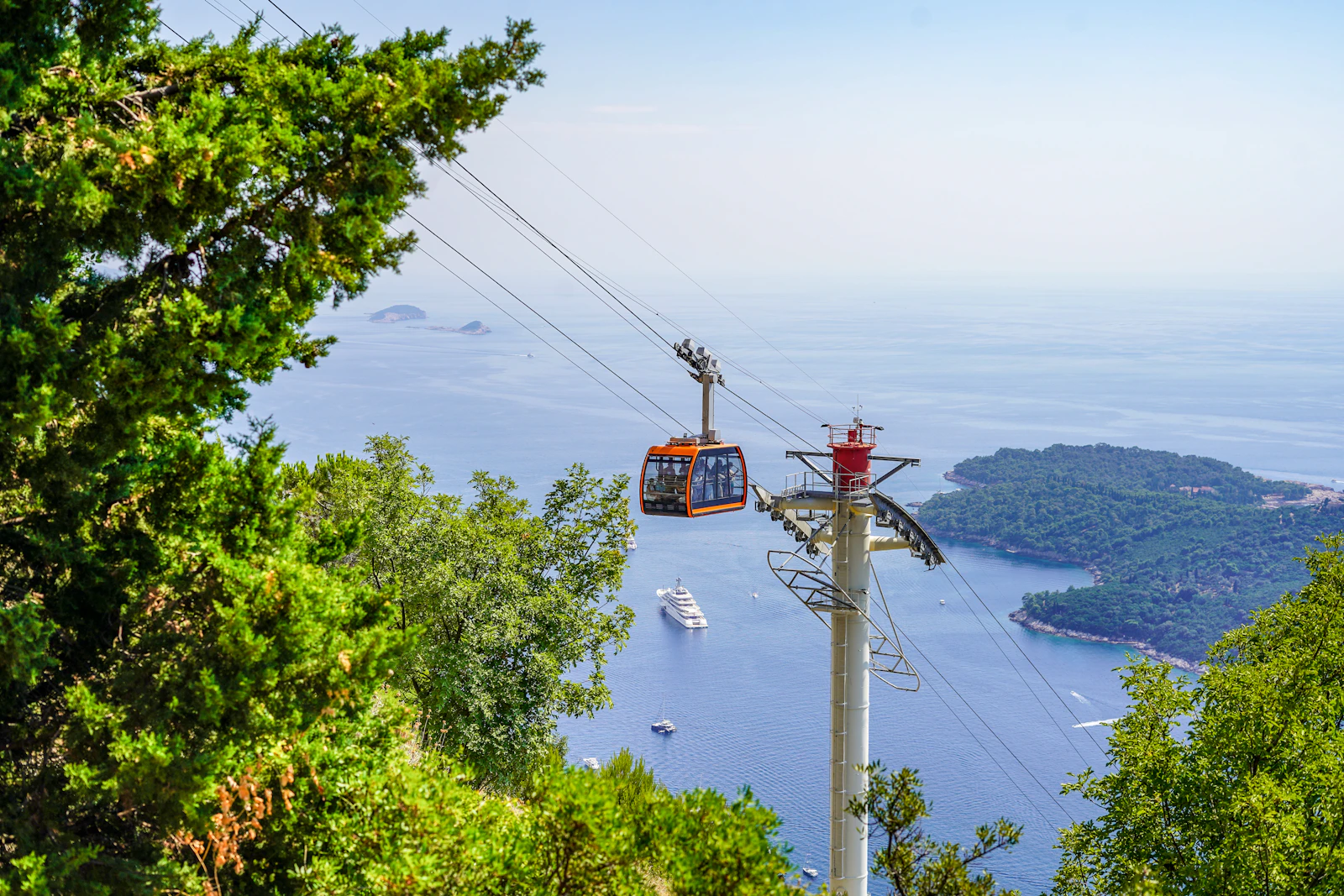 An orange Dubrovnik cable car gondola climbing Mount Srd with Lokrum island and the Adriatic Sea behind
