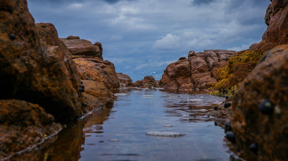 a body of water surrounded by rocks under a cloudy sky