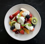 A bright yellow ceramic plate filled with fresh fruit, placed on a linen cloth near a window.