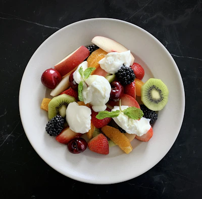 A colorful plate with fresh fruit slices, a croissant, and a small bowl of yogurt.