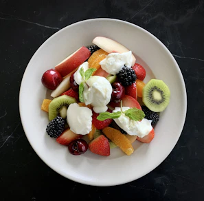 A bright yellow ceramic plate filled with fresh fruit, placed on a linen cloth near a window.