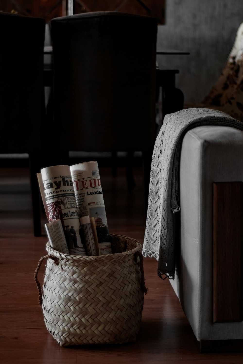 a basket of newspapers sitting on the floor next to a couch