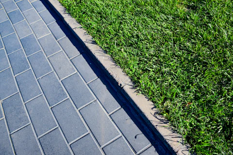 Uneven grass beside a stone pathway before edging and strimming, showing where the lawn needs a clea