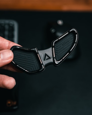 A hand is holding a black ergonomic object with a sleek design. The object has curved edges, and the text 'DELTAHUB' and 'CARPIO' are visible on its surface. The background is dark, providing contrast to the object being held.