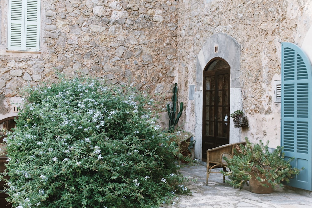 a stone building with blue shutters next to a bush