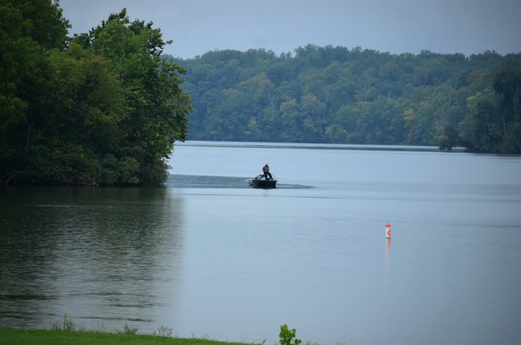 An angler casting from a small boat in the middle of a calm lake at sunrise.