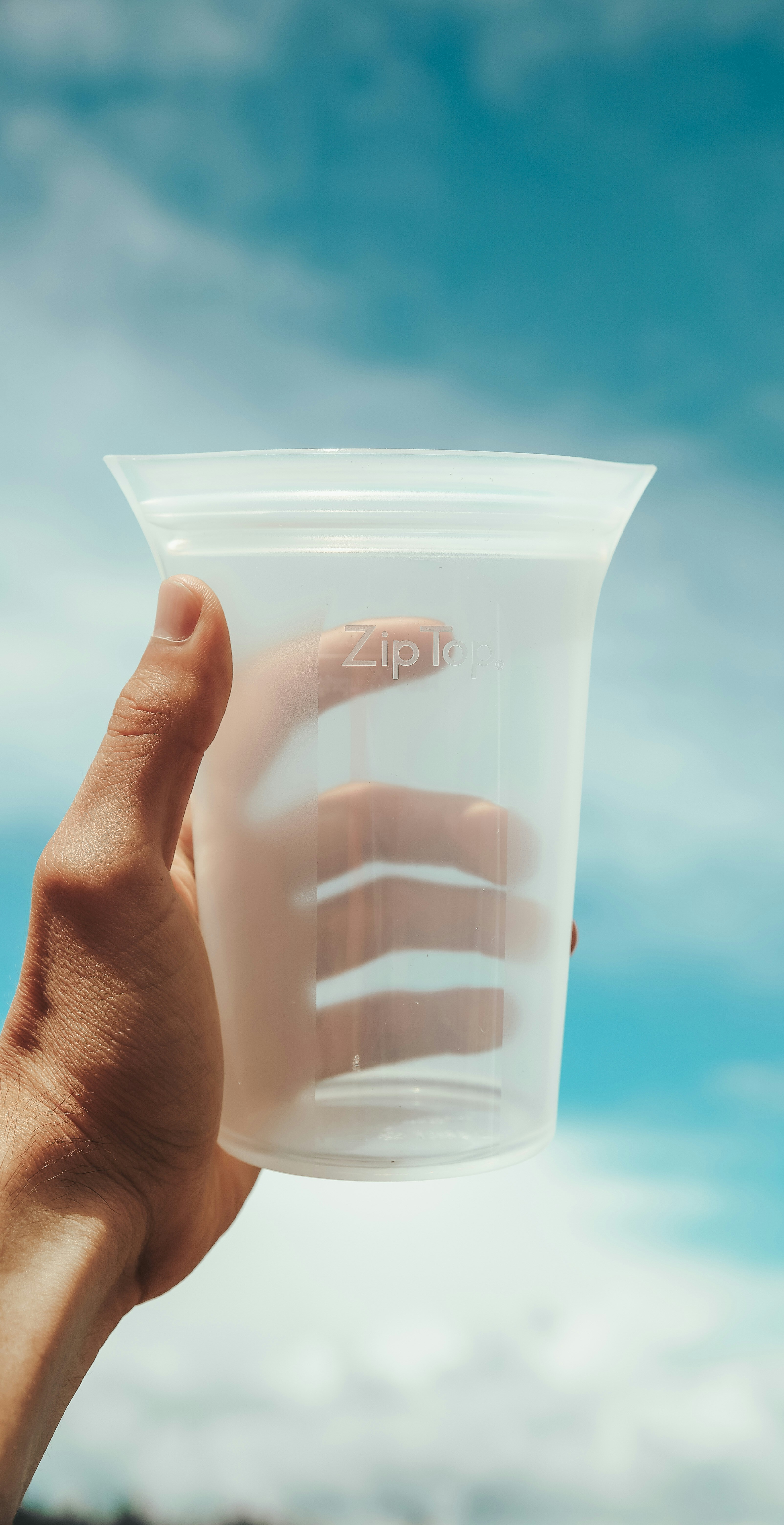 eine Hand, die einen Plastikbehälter mit blauem Himmel im Hintergrund hält