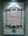 An ornate, teal-colored wooden frame hangs on a textured, cream-colored wall. The frame features intricate, decorative carvings at the top and bottom, adding a classic and elegant touch to the overall appearance.