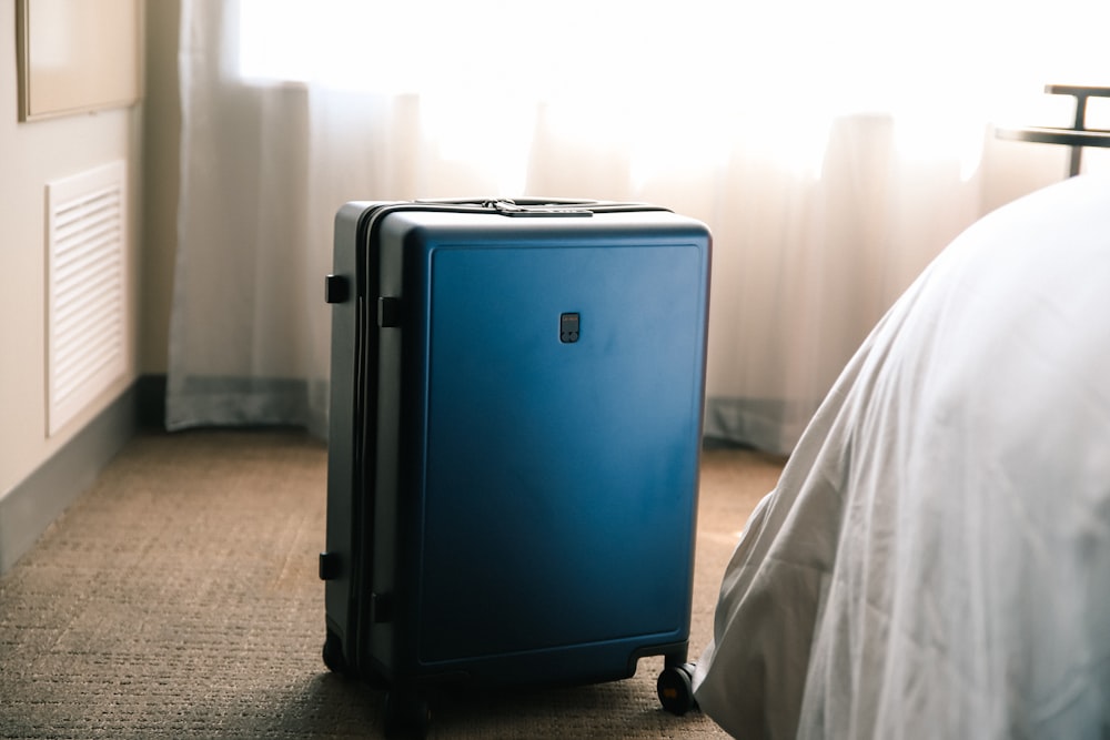 ベッドの隣の床に座っている青いスーツケース