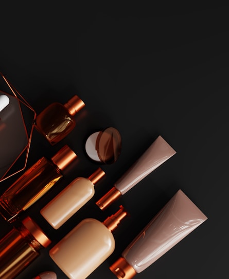 Close-up of elegant amber brown personal care bottles with emerald green and gold labels arranged on a dark surface.