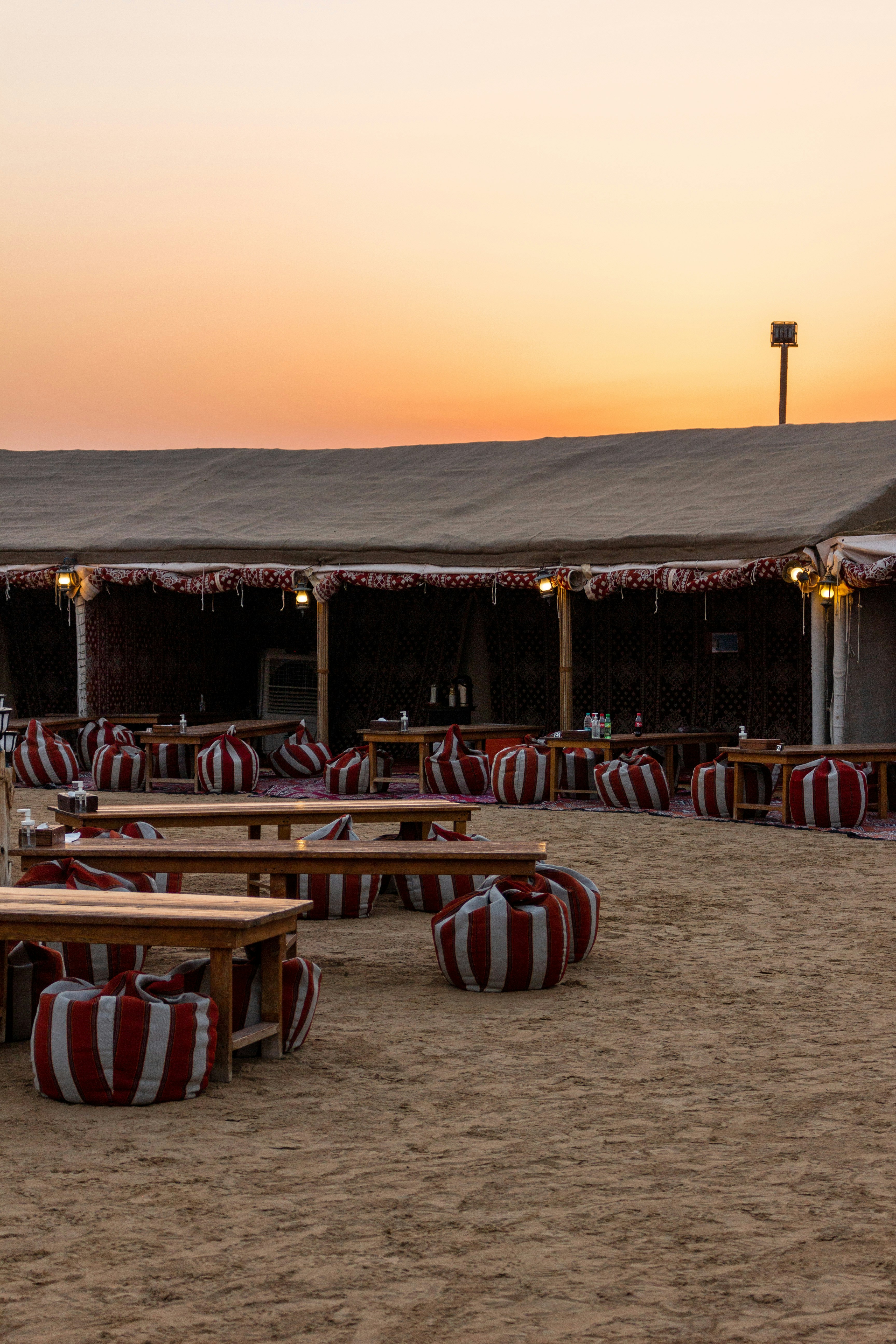 Luxury desert camp tent interior, warm amber lighting, draped fabrics, low wooden furniture, desert through open flap at dusk