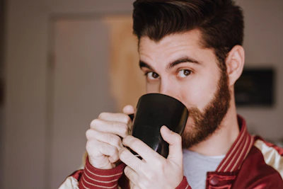 Close-up of a grumpy man’s gentle smile as he holds a vintage coffee mug.