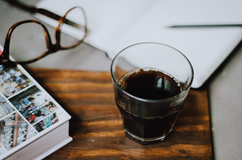 a glass of coffee next to a magazine and a pair of glasses