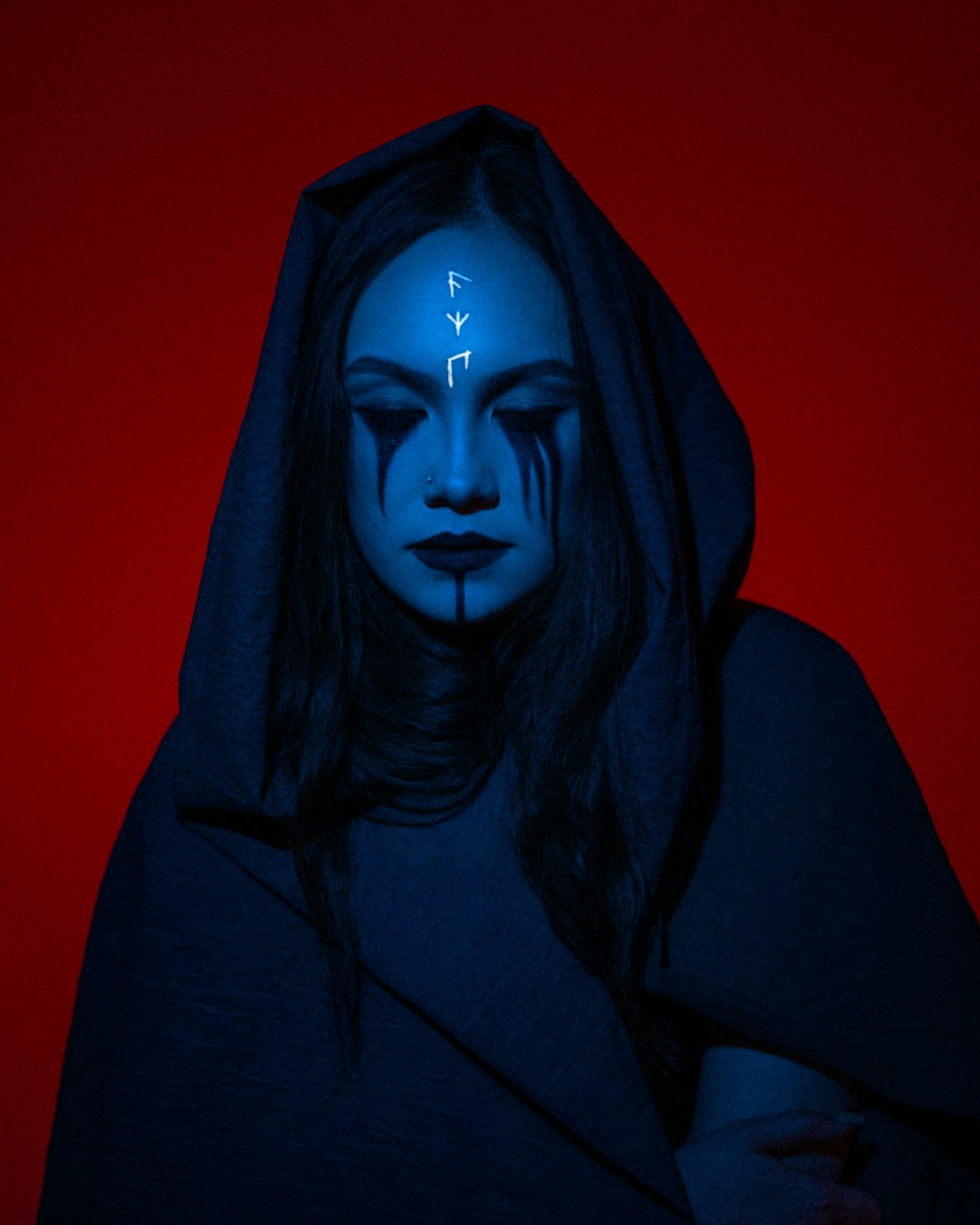 Une femme avec un maquillage bleu et un sweat à capuche avec des flèches peintes sur son visage