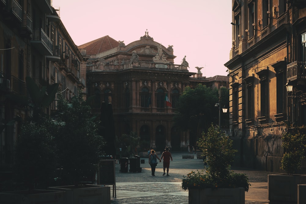 a couple of people walking down a street next to tall buildings