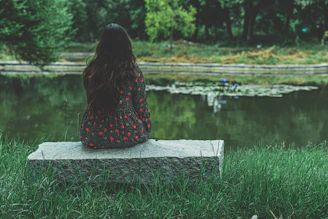 a woman sitting on a rock looking at a pond