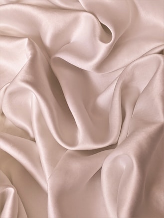Smooth, flowing folds of shiny, champagne-colored satin fabric create an elegant, luxurious texture.