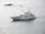 A large white yacht is sailing through calm waters, with small rocky formations and a buoy visible in the background. The sky appears overcast, casting a serene, grey light over the scene.