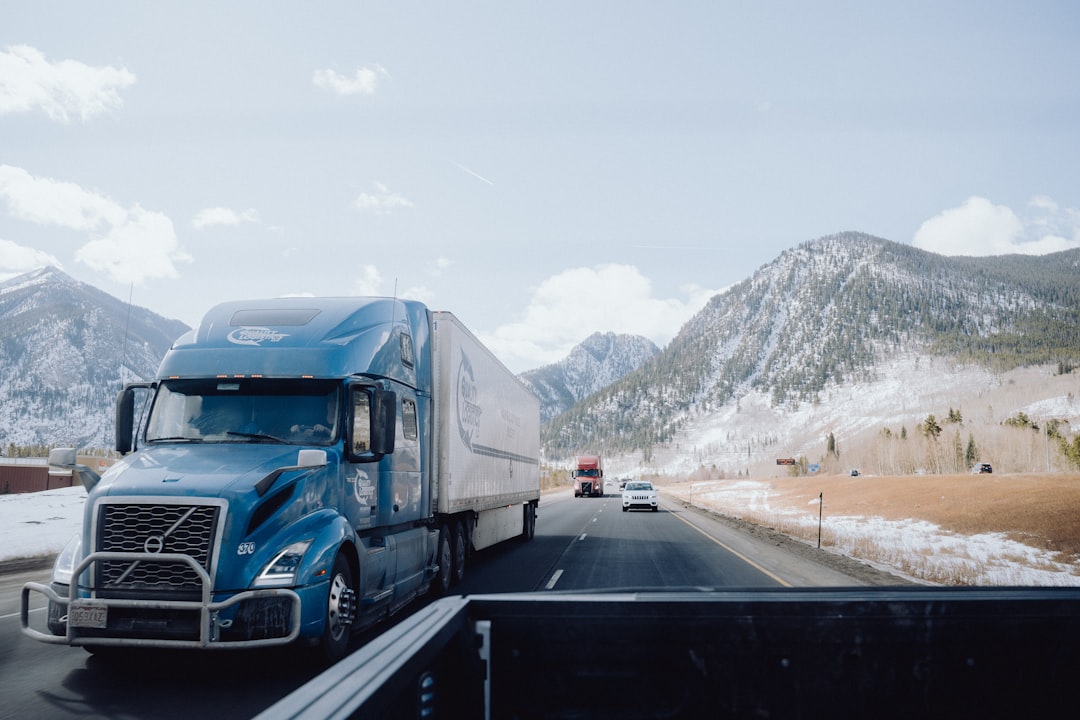 a blue semi truck driving down a mountain road,