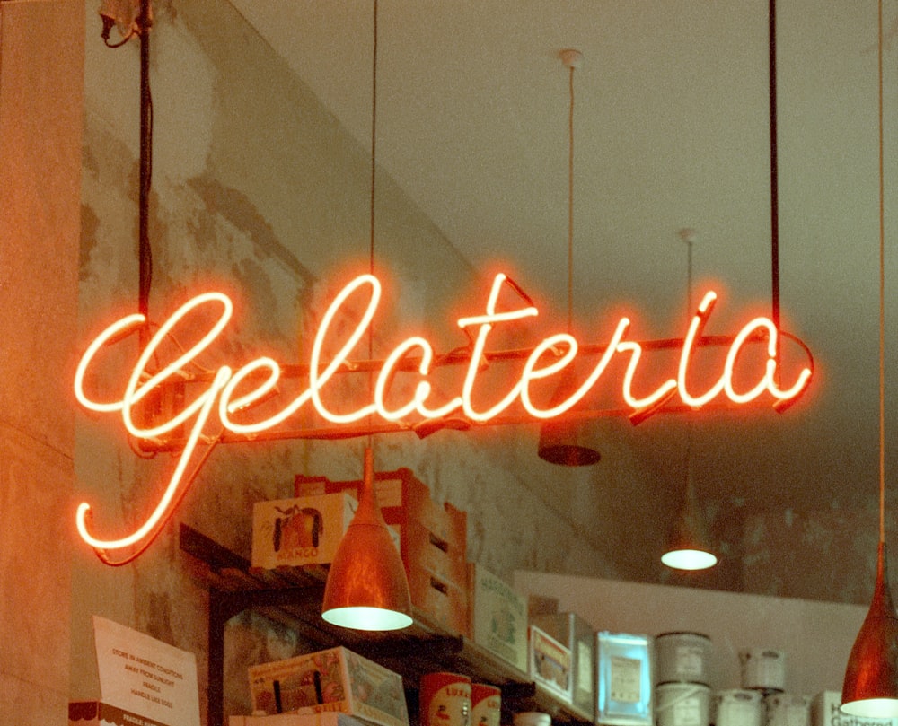 a neon sign that reads gelaterria hangs above a counter