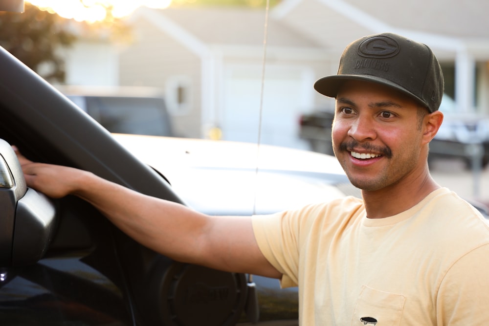 Un hombre con bigote y gorra de béisbol asomándose por la ventanilla de un coche