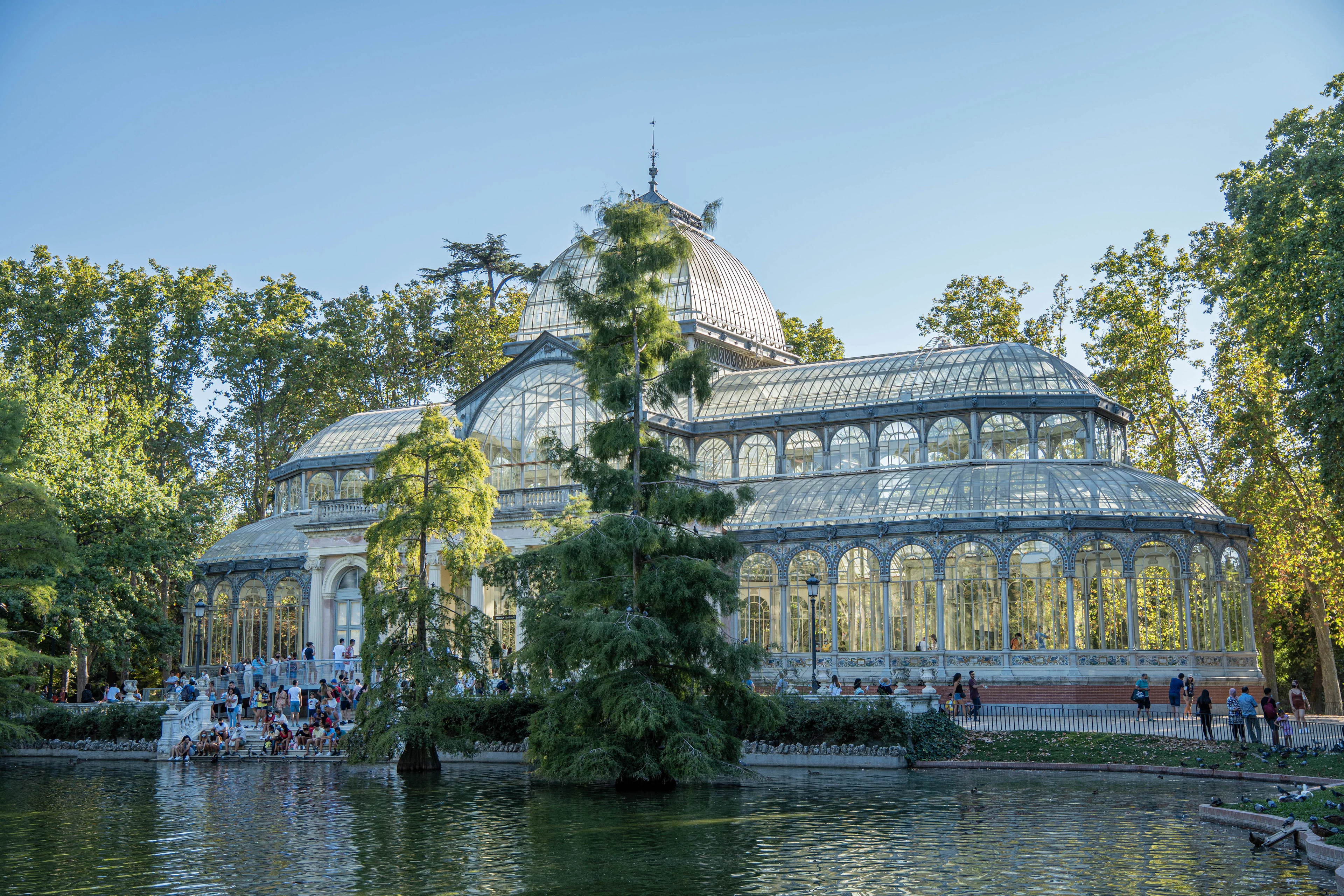 The glass-and-iron Palacio de Cristal standing above its pond in Madrid's Retiro Park, surrounded by trees